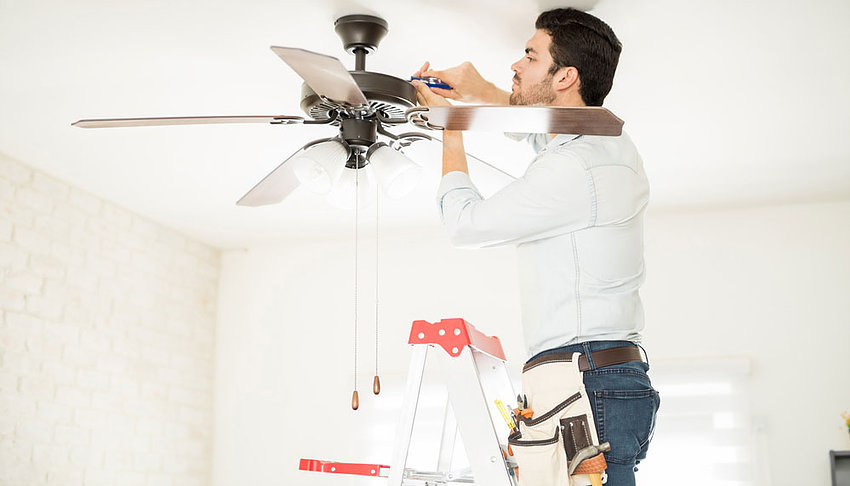 Our electrician repairing a ceiling fan in the living room while standing on a ladder.